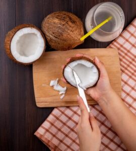 top view female hands holding coconut one hand cutting other hand wooden kitchen board with coconuts glass water checked tablecloth black 141793 17228